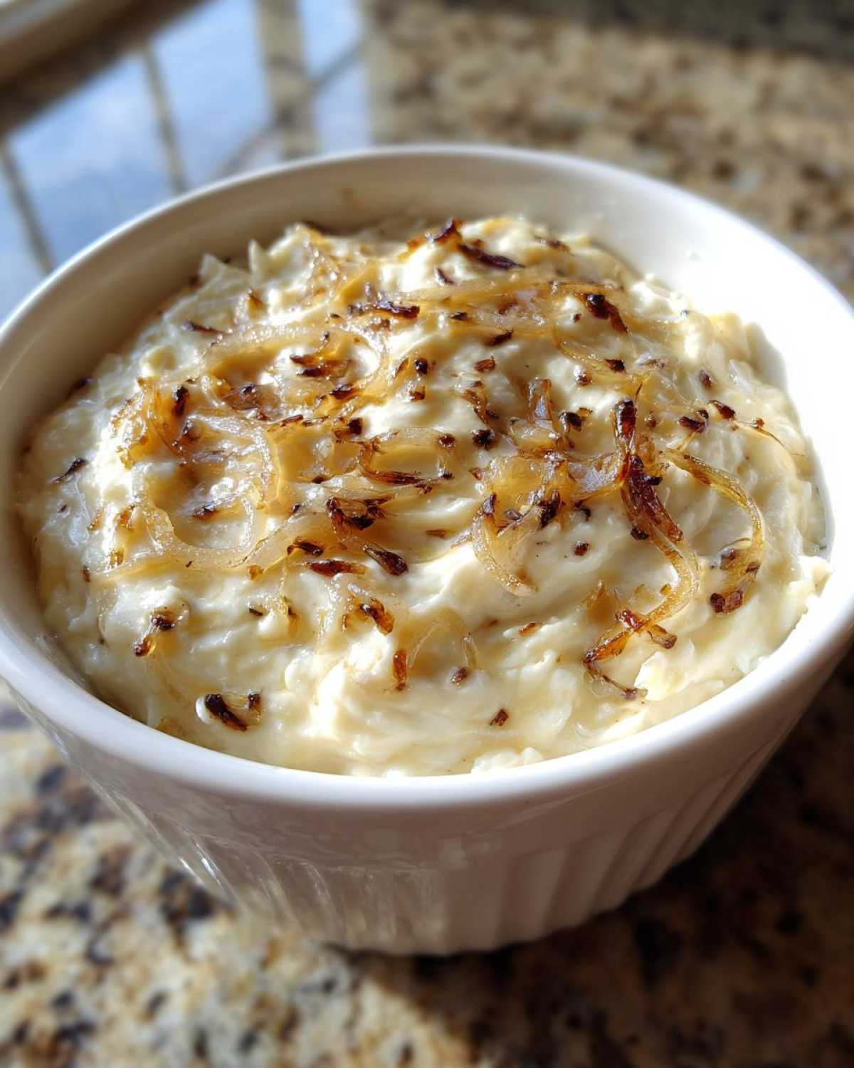 Close-up of creamy caramelized onion dip in a white bowl, topped with golden caramelized onions.