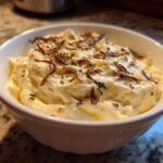 Close-up of creamy caramelized onion dip topped with crispy onions and herbs in a white bowl.
