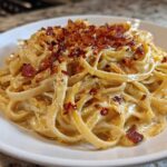 A close-up of creamy fettuccine noodles tossed in sauce, topped with crispy bacon bits and caramelized onion pasta.