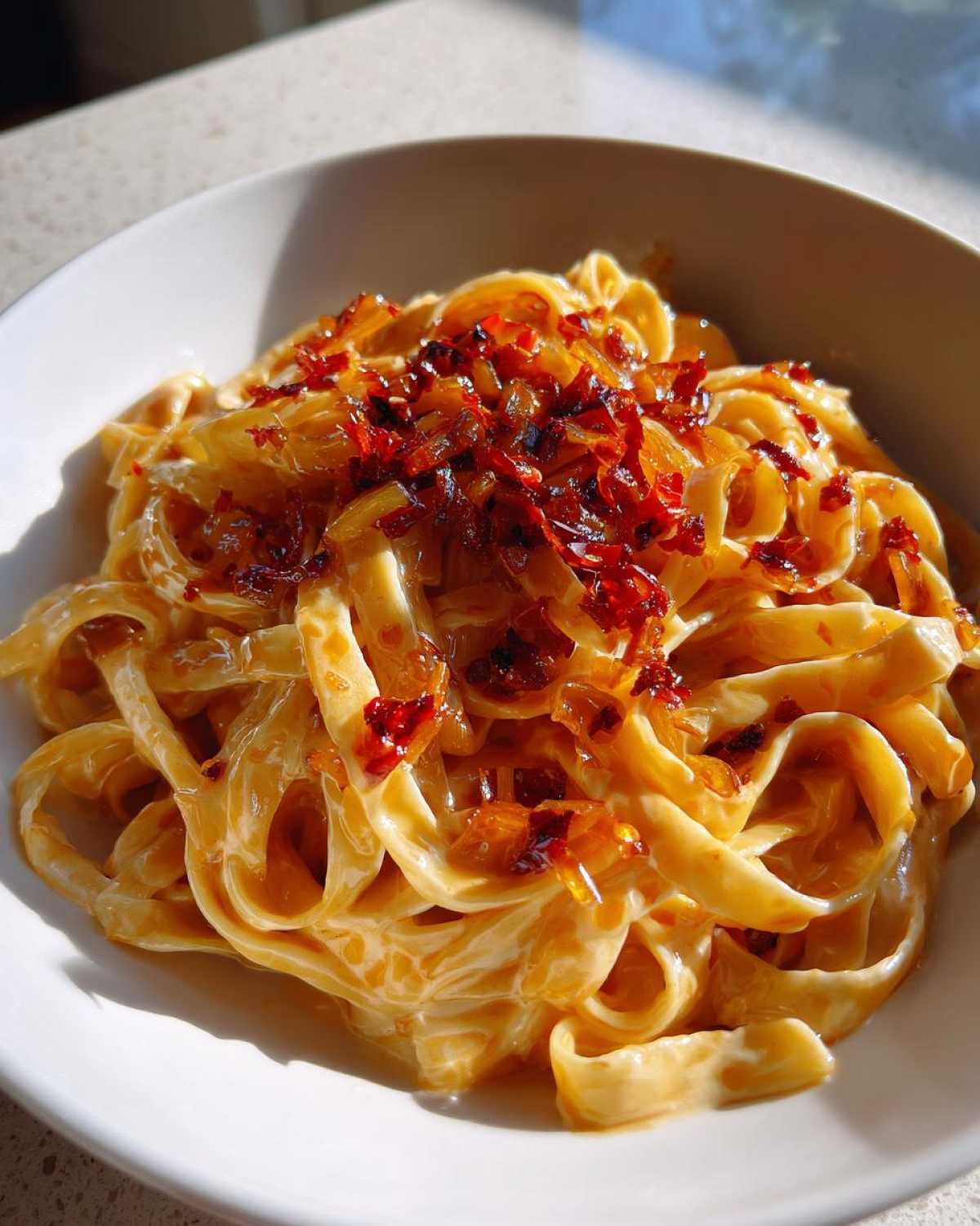 Close-up of creamy fettuccine tossed in sauce and topped with caramelized onion pasta mixture.