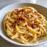 Close-up of creamy fettuccine coated in sauce, topped with crispy caramelized onion pasta garnish.