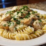 Close-up of creamy chicken pasta featuring chunks of chicken breast and fusilli pasta, topped with fresh parsley.