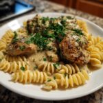 Close-up of creamy chicken pasta featuring grilled chicken pieces over fusilli pasta, topped with rich sauce and fresh parsley.