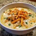 Close-up of a bowl of creamy chicken tortilla soup, generously topped with shredded chicken, cheese, and crispy tortilla strips.