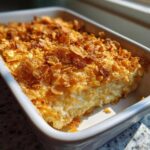 A close-up of creamy funeral potatoes recipe baked in a white casserole dish with a golden, crunchy cornflake topping.
