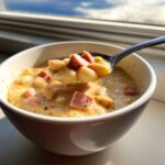 A spoonful of creamy ham bean soup lifted from a white bowl, showing white beans and diced ham.