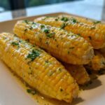 Several bright yellow ears of cooked corn covered in melted honey butter and fresh parsley.