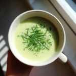 Overhead view of a creamy leek soup in a white mug, garnished generously with chopped fresh chives.