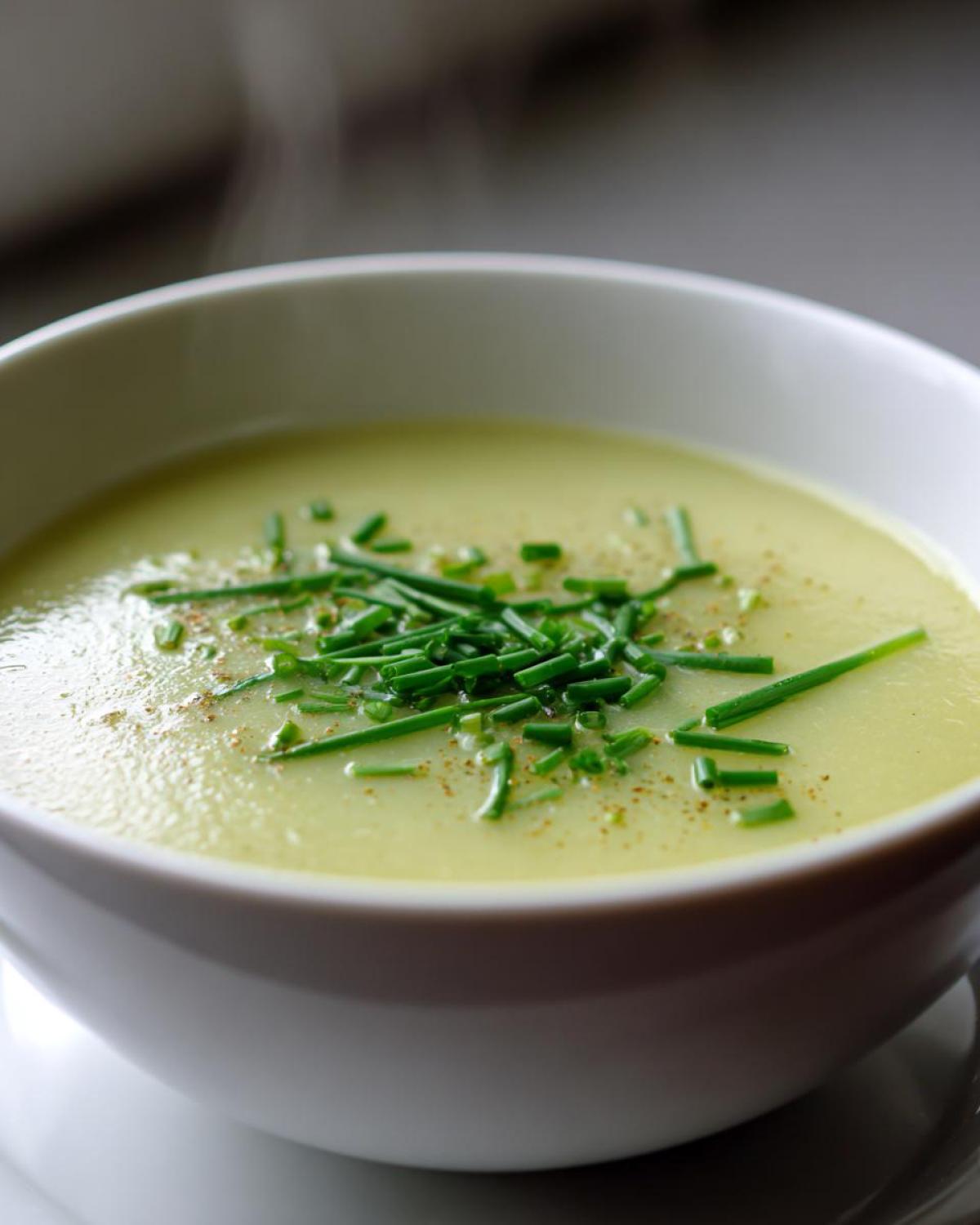 Close-up of a bowl of hot, creamy leek soup garnished with fresh chopped chives and pepper.
