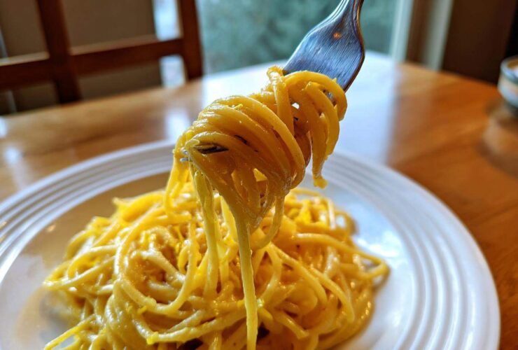 A fork lifting a twirled portion of bright yellow Creamy Lemon Pasta from a white plate.