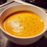 Close-up of a bowl of rich, creamy orange cauliflower soup, seasoned with black pepper.