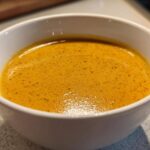 Close-up of a rich, orange-hued, creamy cauliflower soup served in a white bowl.