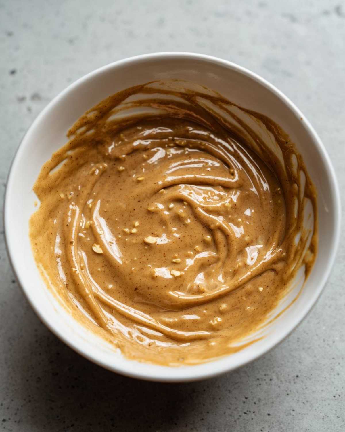 Overhead view of creamy peanut sauce with visible crushed nuts in a white bowl.