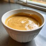 Close-up of a thick, creamy peanut sauce with visible spices in a white ribbed bowl.