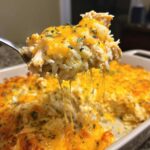 A spoonful of creamy rice casserole with shredded chicken and melted cheddar cheese being lifted from the baking dish.