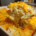 A spoonful of creamy rice casserole being lifted, showing melted cheese strings stretching back to the dish.