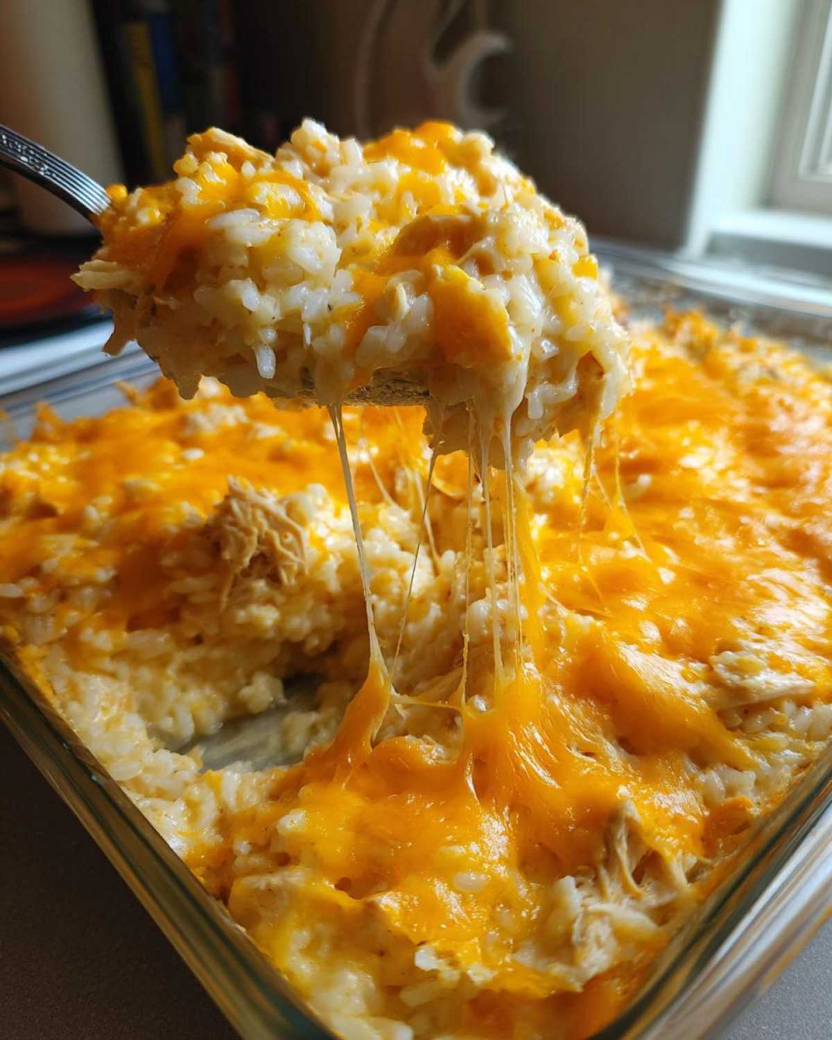 A spoonful of creamy rice casserole topped with melted cheddar cheese showing long cheese pulls.