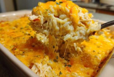 A spoonful of creamy rice casserole being lifted, showing melted cheese strings stretching back to the dish.