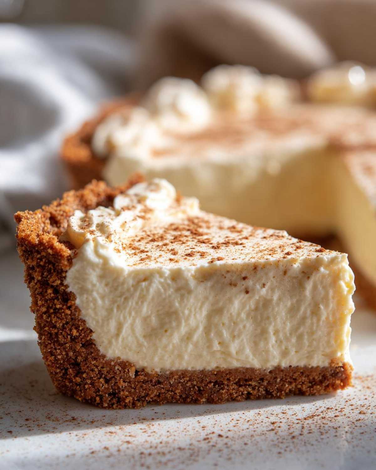 Close-up of a thick slice of creamy eggnog pie with a graham cracker crust, dusted with cinnamon.