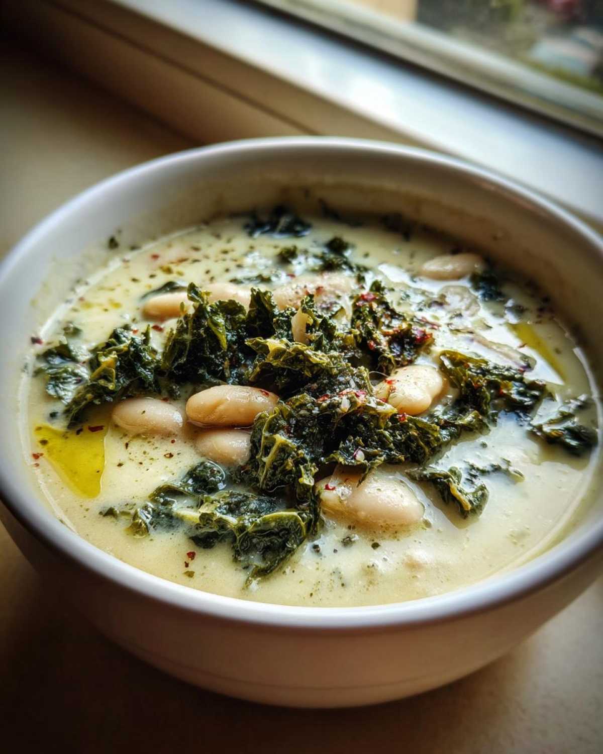Close-up of a creamy Tuscan white bean soup topped with dark green kale and red pepper flakes.