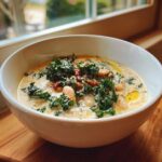 A close-up of a bowl of creamy Tuscan white bean soup topped with fresh kale, white beans, and sun-dried tomatoes.
