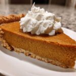 A close-up of a rich slice of easy pumpkin pie topped with a dollop of whipped cream.