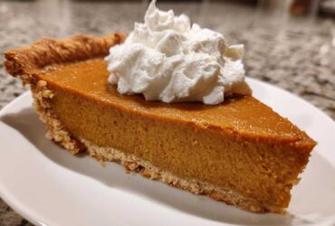 A close-up of a rich slice of easy pumpkin pie topped with a dollop of whipped cream.