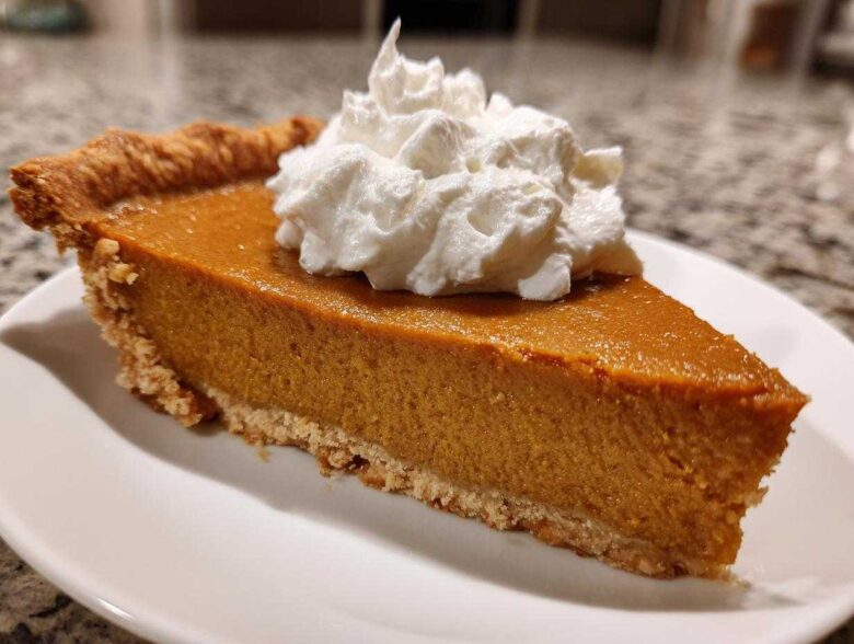 A close-up of a rich slice of easy pumpkin pie topped with a dollop of whipped cream.