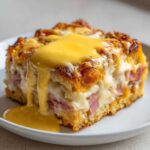 A close-up of a square serving of eggs benedict casserole topped with rich, dripping hollandaise sauce.