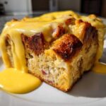 A thick, square slice of baked eggs benedict casserole topped generously with rich, yellow hollandaise sauce.