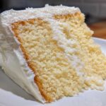 Close-up of a moist cake slice generously topped with fluffy vanilla buttercream frosting.