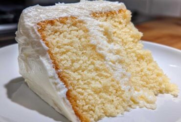 Close-up of a moist cake slice generously topped with fluffy vanilla buttercream frosting.