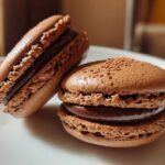 Close-up of two perfectly formed chocolate macarons with rich ganache filling, showcasing their ruffled feet.