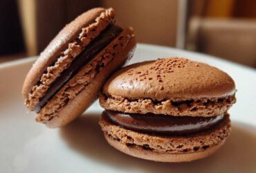 Close-up of two perfectly formed chocolate macarons with rich ganache filling, showcasing their ruffled feet.