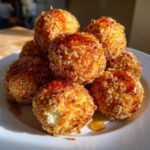 A pile of crispy, golden-brown fried goat cheese balls drizzled with dark honey on a white plate.