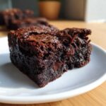 Close-up of a rich, fudgy black bean brownies square on a white plate, showing a melted chocolate chip.