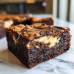A close-up of a fudgy, dark chocolate cream cheese brownies square with a visible cream cheese swirl.