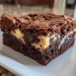 Close-up of a rich, fudgy slice of cream cheese brownies showing the dark chocolate base and swirls of cheesecake.