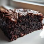Close-up of a thick, fudgy slice of dark chocolate date brownies on a white plate.