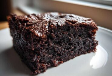 Close-up of a thick, fudgy slice of dark chocolate date brownies on a white plate.
