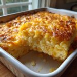 A slice of creamy funeral potatoes recipe with a golden, crunchy cornflake topping in a white baking dish.