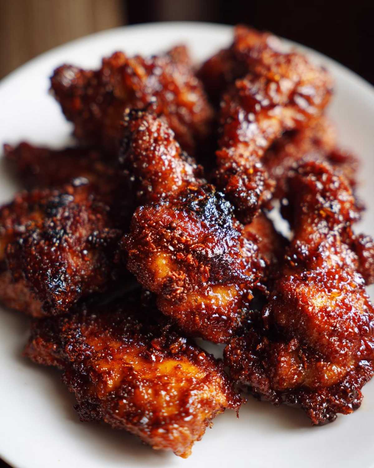 Close-up of crispy, glazed pieces of honey garlic chicken piled on a white plate.