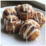 A plate of freshly made, gooey cinnamon roll bites drizzled generously with white vanilla icing.