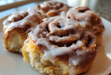 Close-up of three freshly baked, gooey cinnamon roll bites topped with thick white icing.