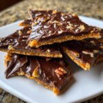 A stack of broken pieces of graham cracker toffee topped with melted dark chocolate and chopped pecans.