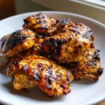 Close-up of perfectly grilled chicken pieces coated in a golden, zesty chicken marinade, showing char marks.