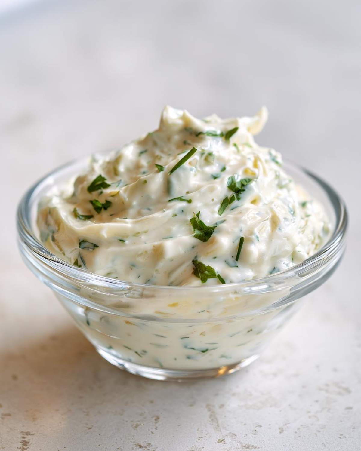 A close-up of creamy, homemade tartar sauce recipe garnished with fresh green herbs in a small glass bowl.