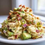 A mound of creamy honey mustard chicken salad mixed with chunks of avocado, red onion, and topped with crispy bacon bits.
