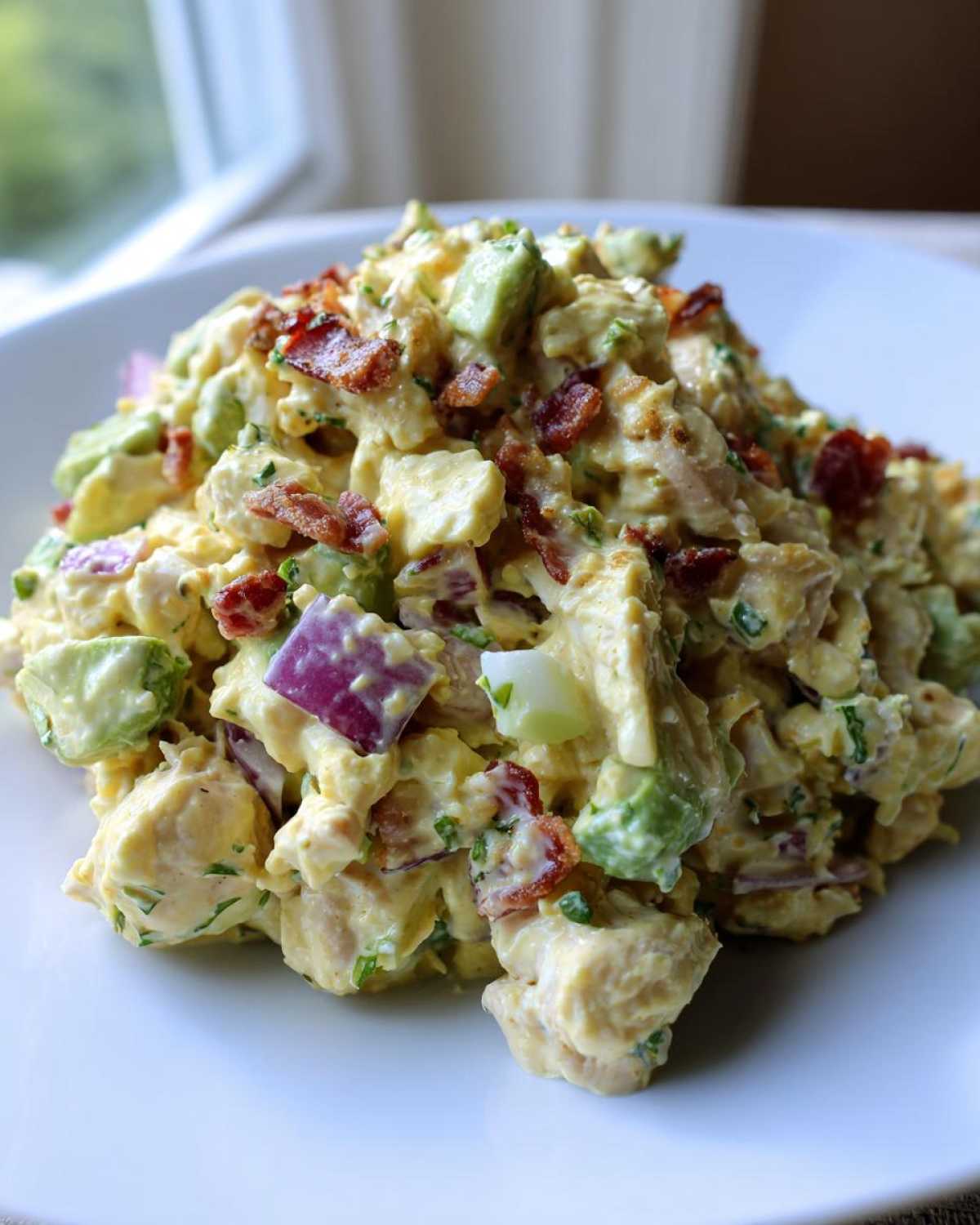 A mound of creamy honey mustard chicken salad mixed with avocado, red onion, and topped with crispy bacon crumbles.