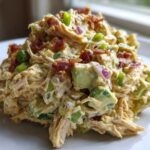 A mound of creamy honey mustard chicken salad mixed with chunks of avocado, red onion, and topped with crispy bacon bits.